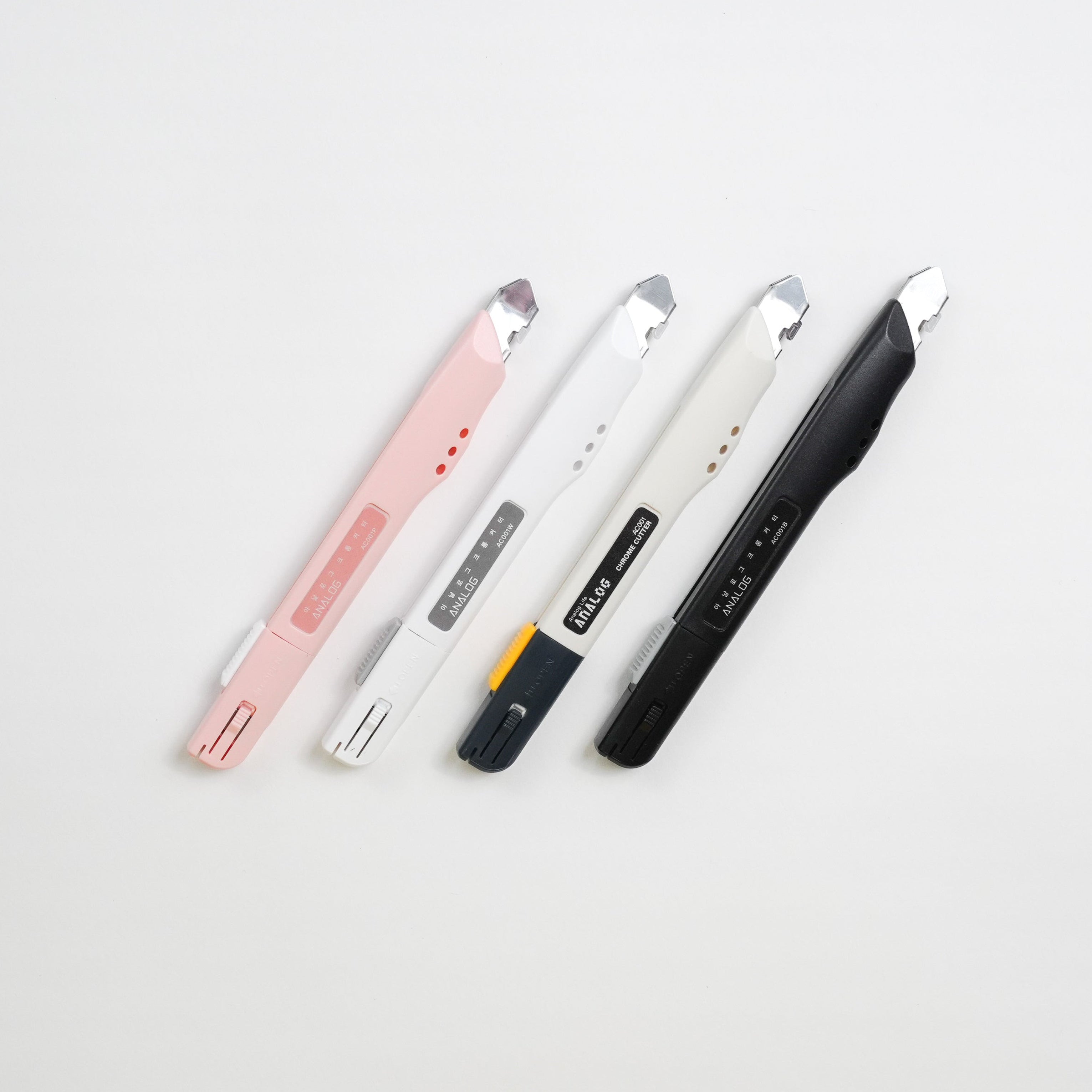Four utility knives in pastel pink, white, and black, arranged diagonally on a clean white background.
