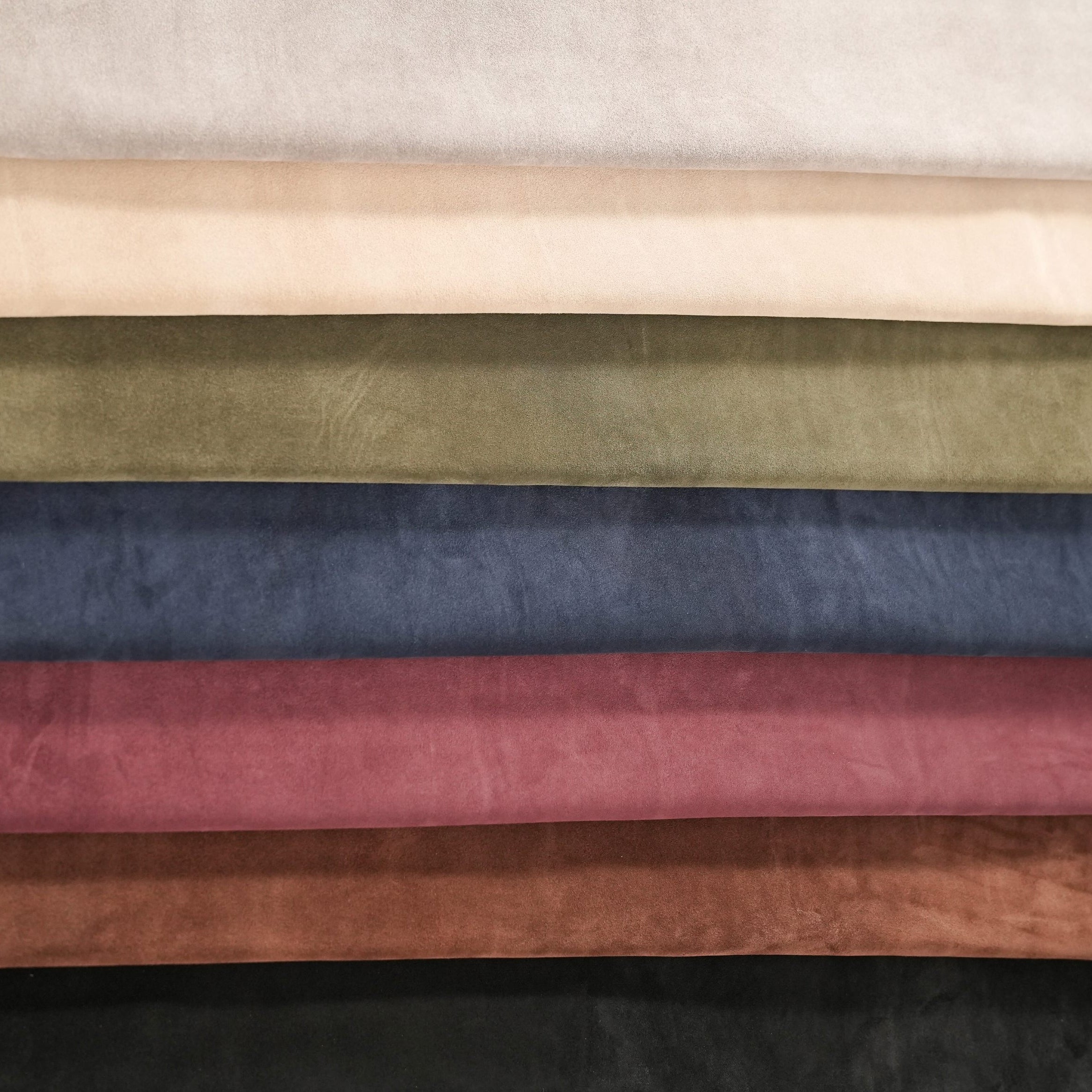 Collection of cowhide leather suede hides in various colors on a neutral background
